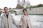 Couple holding hands along Seine River near Notre Dame Cathedral, Paris, France