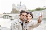 Couple taking self-portrait along Seine River near Notre Dame Cathedral, Paris, France