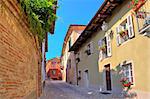 Narrow cobbled street among old brick wall and colorful houses in small town of Guarene in Piedmont, Northern Italy.