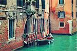 Small boat tied next to old red brick house with wooden balcony on narrow canal in Venice, Italy (toned image).