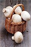 Big Raw mushrooms in Wicker Basket isolated on Rustic Wooden background