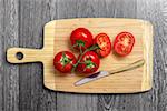 Top view of fresh tomatoes and knife on chopping board on gray table