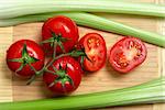 High angle view of bunch of fresh tomatoes and celery sticks on wooden chopping board