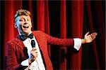 Arts and entertainment in theatre with funny man working as anchorman, standing against red curtains with microphone