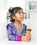 Little Indian girl licking her lips with an ice cream cone in hand, family living lifestyle at home.
