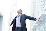 Indian businessman open his arms wide, looking up into the light, modern office building as background, natural sunlight.