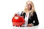 Happy blond women sitting at a table and throwing euro banknotes in a red piggy bank