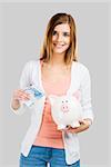 Beautiful woman putting money in a piggy bank, isolated over white background