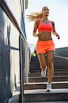 Young female runner moving down city stairway