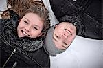 Portrait of teenage girl and her brother lying in snow