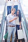 Young couple using cellular phone on escalator