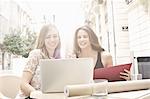 Two young female friends looking at laptop at sidewalk cafe, Valencia, Spain