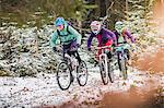 Three female mountain bikers riding through forest in snow