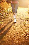 Mature woman jogging on path in sunlight, low section