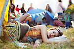 Woman with tiara sleeping in sleeping bag outside tents at music festival