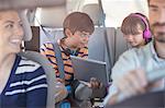 Brother and sister sharing digital tablet in back seat of car