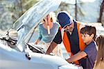 Boy watching roadside mechanic check car engine