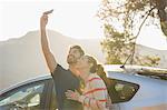 Happy couple taking self-portrait with camera phone outside car