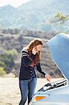 Woman talking on cell phone with automobile hood raised at roadside