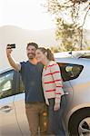 Couple taking self-portrait with camera phone outside car