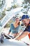 Woman watching roadside mechanic check car engine