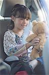 Girl with teddy bear in back seat of car