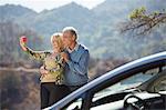 Senior couple taking self-portrait at roadside outside car