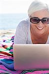 Happy woman using laptop on beach