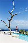 Woman standing on poolside balcony overlooking ocean