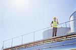 Worker using walkie-talkie on platform next to silage storage towers