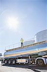 Worker standing on platform above stainless steel milk tanker