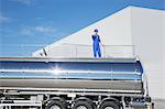 Worker talking on cell phone on platform above stainless steel milk tanker