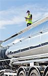 Worker using digital tablet on platform above stainless steel milk tanker