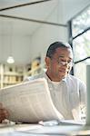 Senior man reading newspaper and using laptop