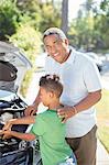 Portrait of smiling grandfather working on car engine with grandson