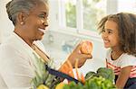 Happy grandmother giving apple to granddaughter in kitchen