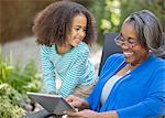 Grandmother and granddaughter using digital tablet on patio