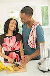 Happy couple slicing fruit next to blender in kitchen