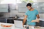 Man with newspaper using laptop in kitchen