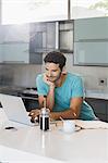 Man drinking coffee and using laptop in kitchen