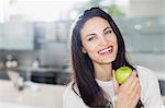 Portrait of smiling woman eating apple in kitchen