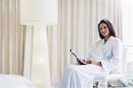 Portrait of smiling woman in bathrobe reading newspaper