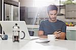 Man texting with cell phone at kitchen table