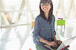 Happy casual businesswoman using laptop in sunny office