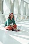 Portrait of confident casual businesswoman using laptop on floor in sunny office