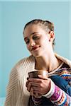 Close-up portrait of teenage girl holding mug with eyes closed, studio shot on blue background