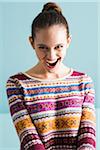 Close-up portrait of teenage girl with hair in bun, looking at camera and smiling with open mouth, studio shot on blue background