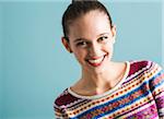 Close-up portrait of teenage girl, looking at camera and smiling, studio shot on blue background