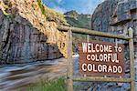 welcome to colorful Colorado roadside wooden sign with a canyon and whitewater river in background