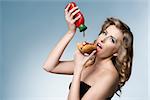 cute blonde lady with fashion style eating hot-dog and putting tomato ketchup on. Glutton woman.